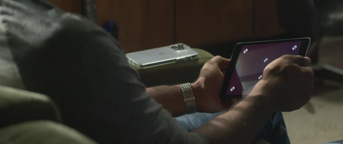 Man sitting on couch near smartphone rotates a tablet back and forth in his hands