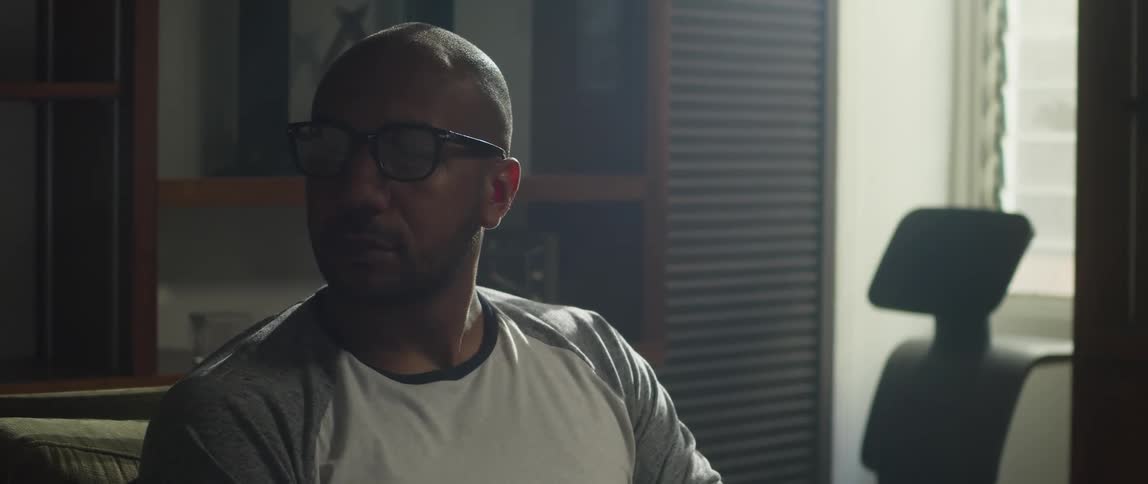 Man with shaved head glasses and sweatshirt sitting on couch looks around in living room at home
