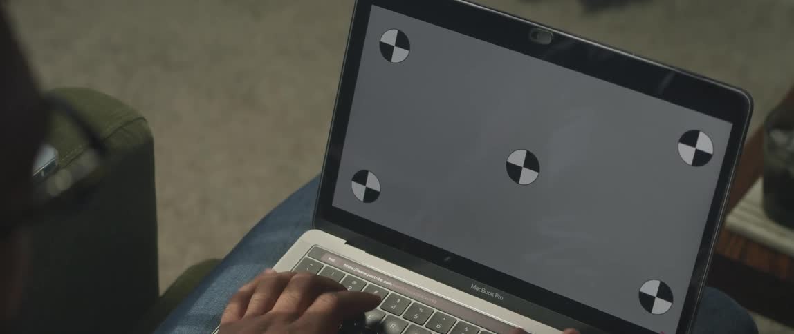 Man with glasses types on macbook pro laptop sitting on green couch