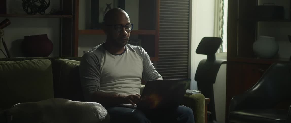 There is a man that is sitting on his couch and working on a laptop