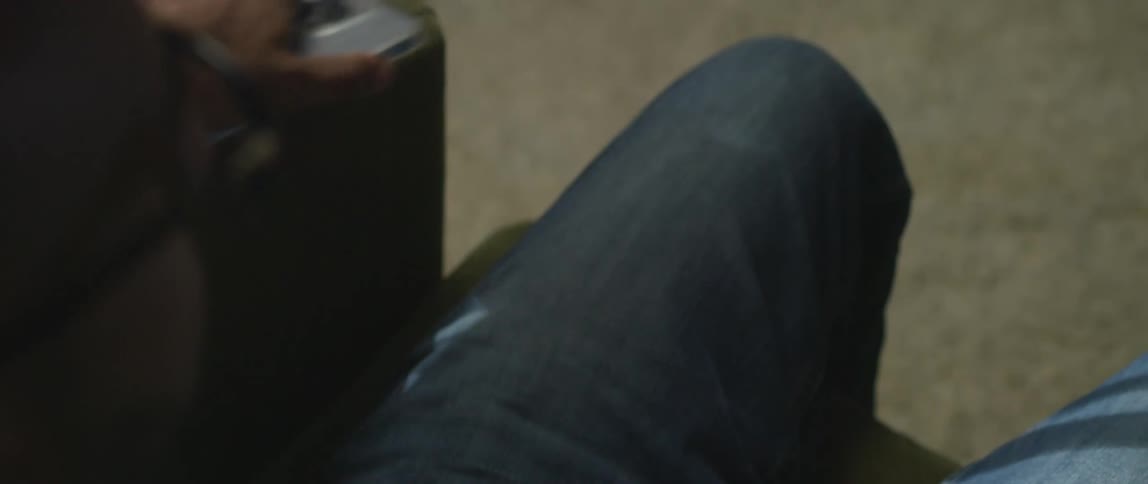 A man is sitting down holding a smart phone with white symbols on the screen and he sets it down on the arm of the couch