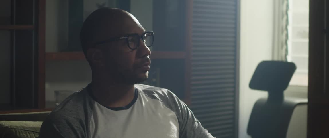 A man sits at home and contemplates as he lets out a long breath