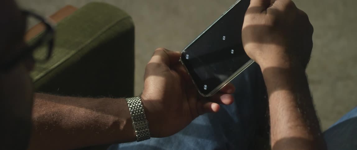 A man turns his cell phone back and forth as he plays a game on it