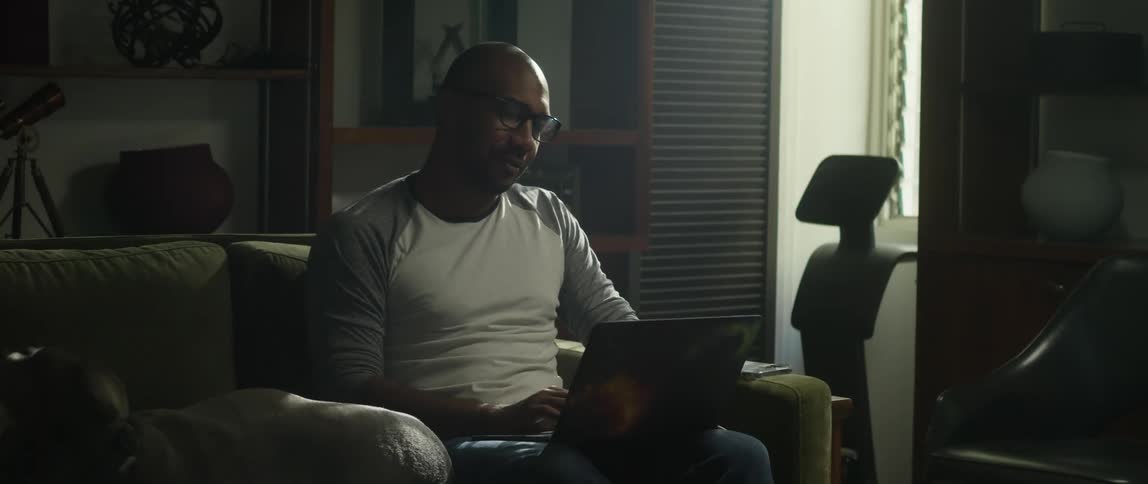 Man stops typing briefly to pet the dog lying on the couch next to him