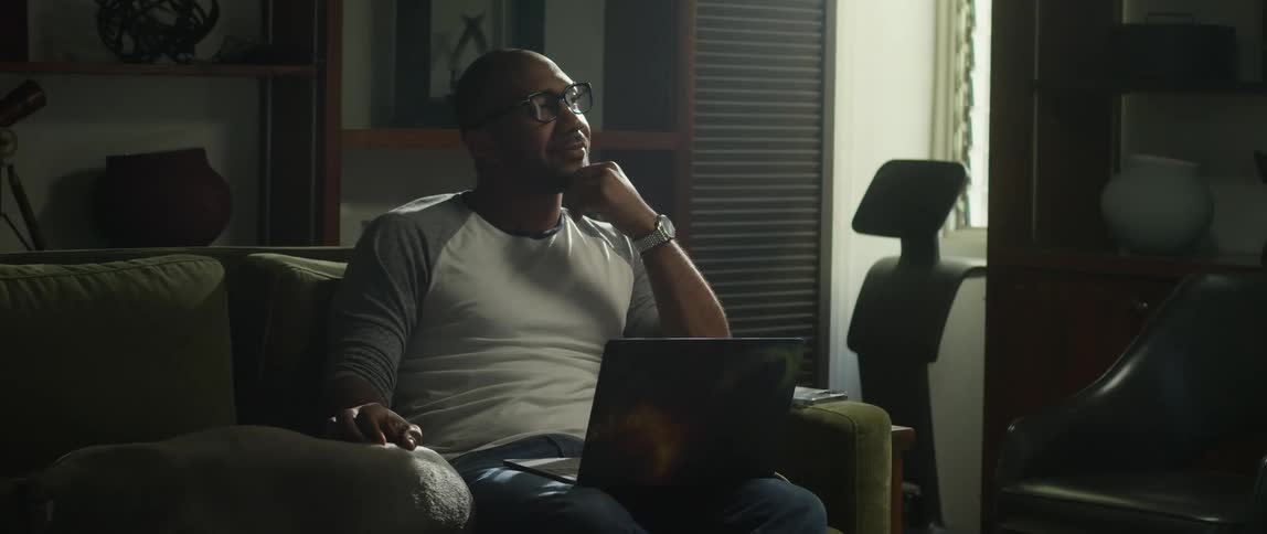 A man pauses work to think and pet his dog then goes back to his laptop