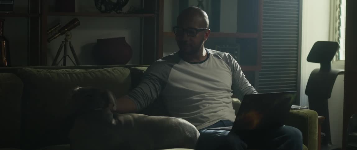 A man is sitting on the couch typing on a laptop computer and his dog is lying next to him