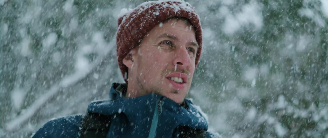 A man standing in the falling snow near trees and branches