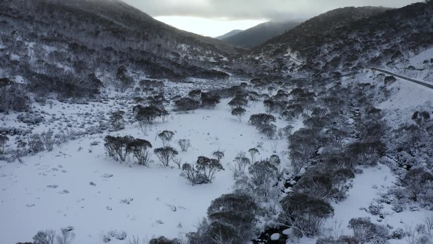 Stream roughly parallels road through snow covered and frozen valley leading to misty mountains on the horizon