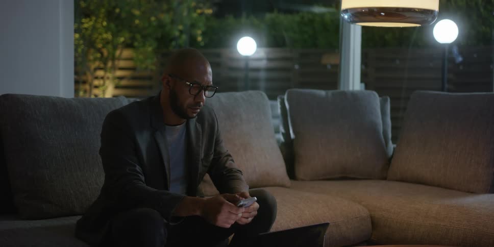 A man is sitting on his living room couch using his smart phone