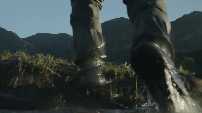 The feet of a man walking across a river