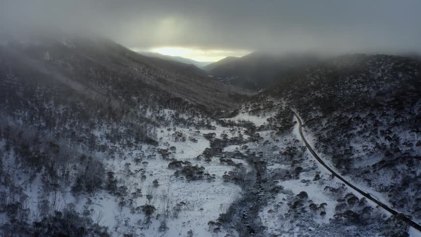 Heavy gray cloud cover over snow dusted mountain valley stream and road