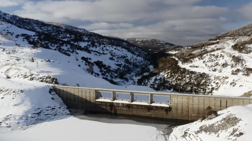 The guthega dam on a frozen lake and between snow covered slopes
