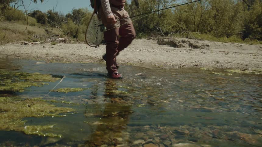 A man is walking on rocks in clear shallow water with his fishing pole