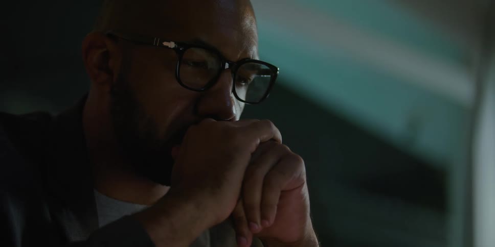 Mans eyeglasses reflect computer screen light as he thinks and works