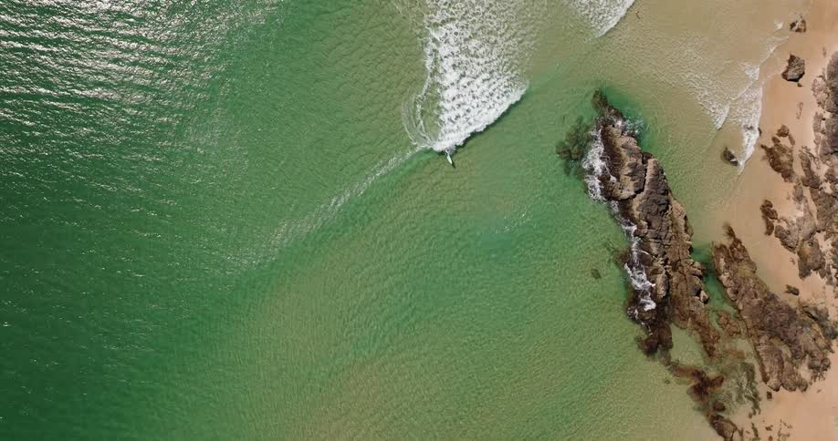 Aerial view of surfer riding a ocean wave on surfboard near the beach
