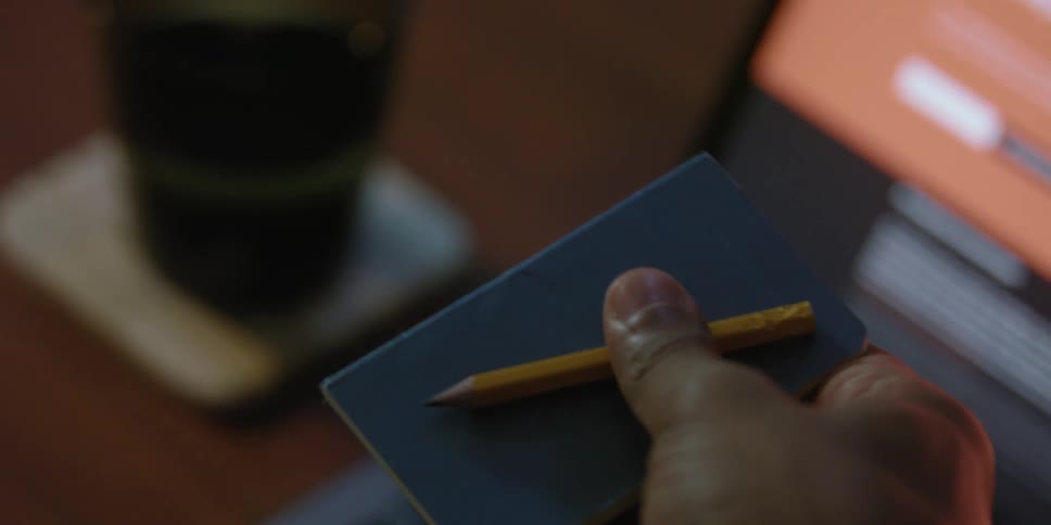 Close up view of a person picking up a notebook from a table and putting it in their pocket