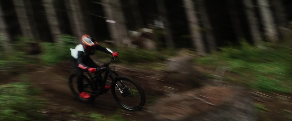 A cyclist repeatedly goes airborne while riding a bicycle along a dirt trail through a woodland during the day