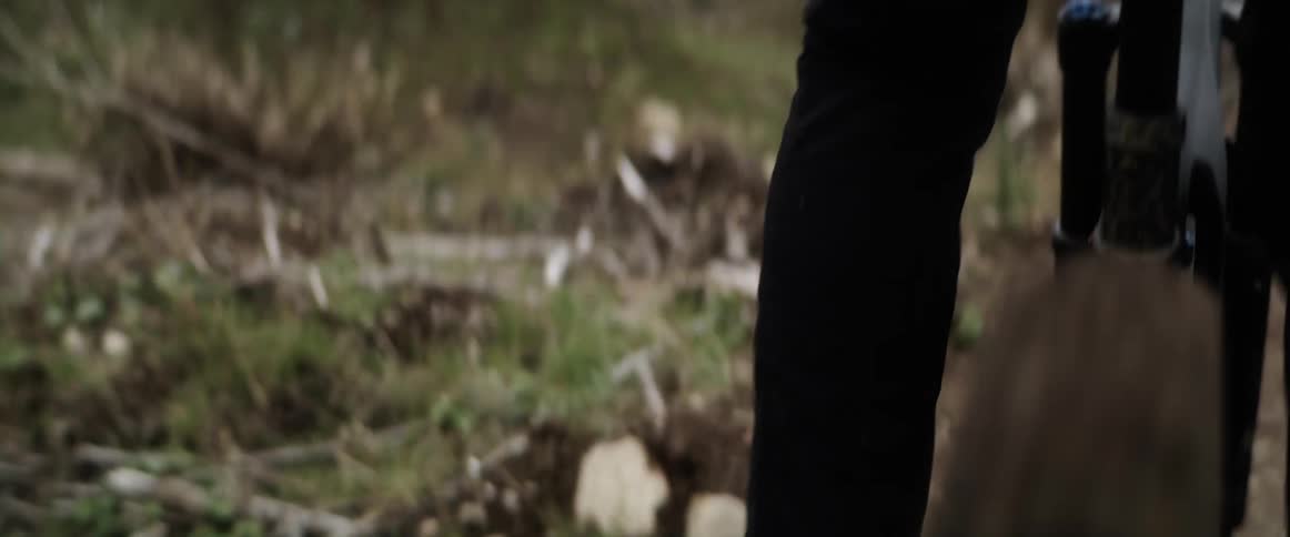 Person with black pants and a pair of sneakers pedals bicycle on forest track