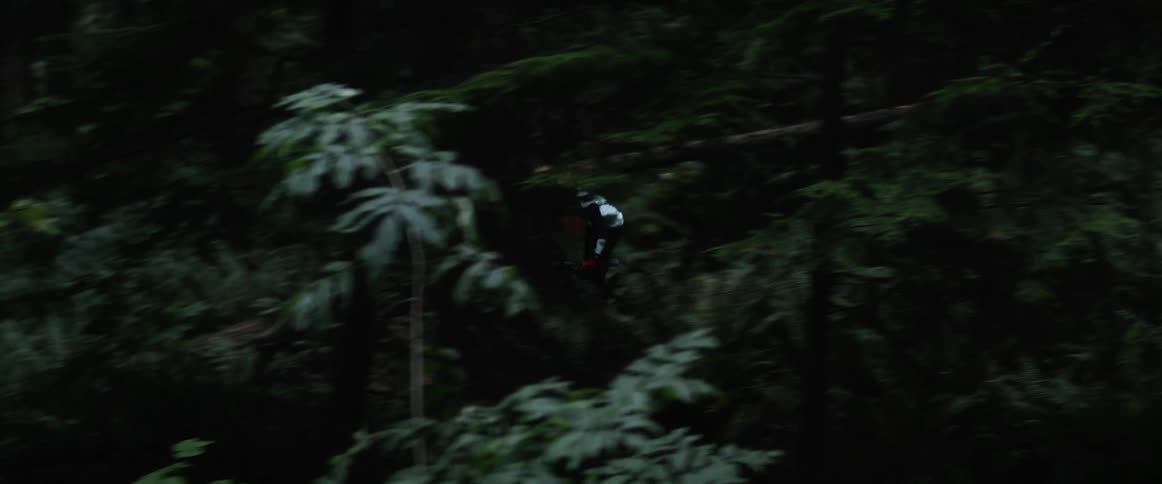 A teenager is riding a mountain bike on a trail and around the bend through a forest of trees