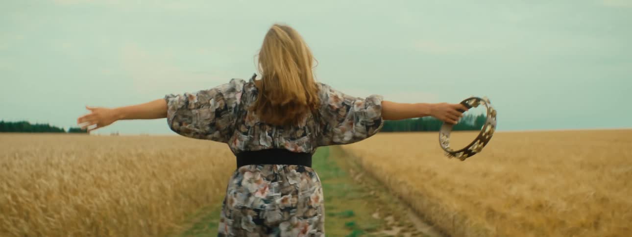 Young woman wearing a dress runs through a field with a tambourine