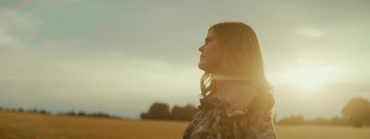 Woman walks past wheat field playing a tambourine