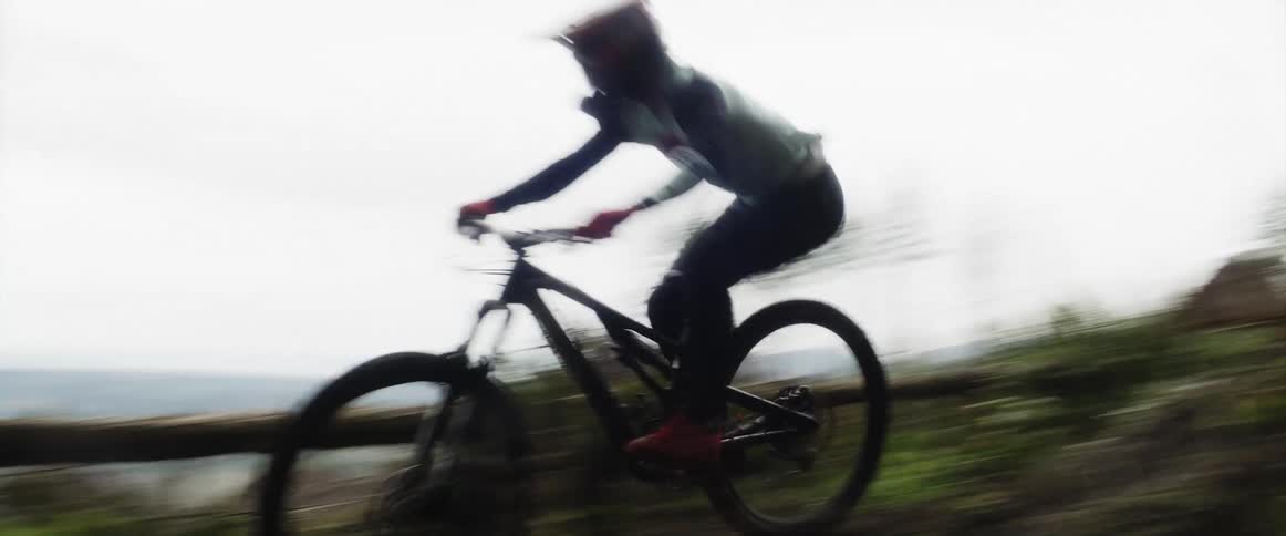 Cyclist rides mountain bike through clearing in forest making a jump off a dirt mound