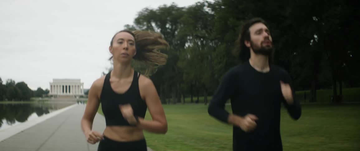 A man and woman run down a trail near a monument