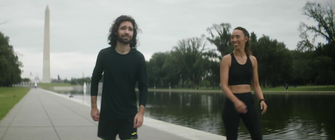 A man and woman talk as they stretch next to a river in a public park and then start to jog