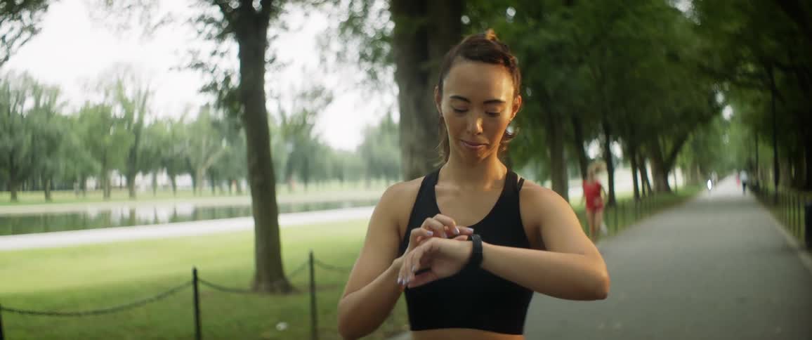 A woman standing on a park path checking her watch waiting for her workout partner