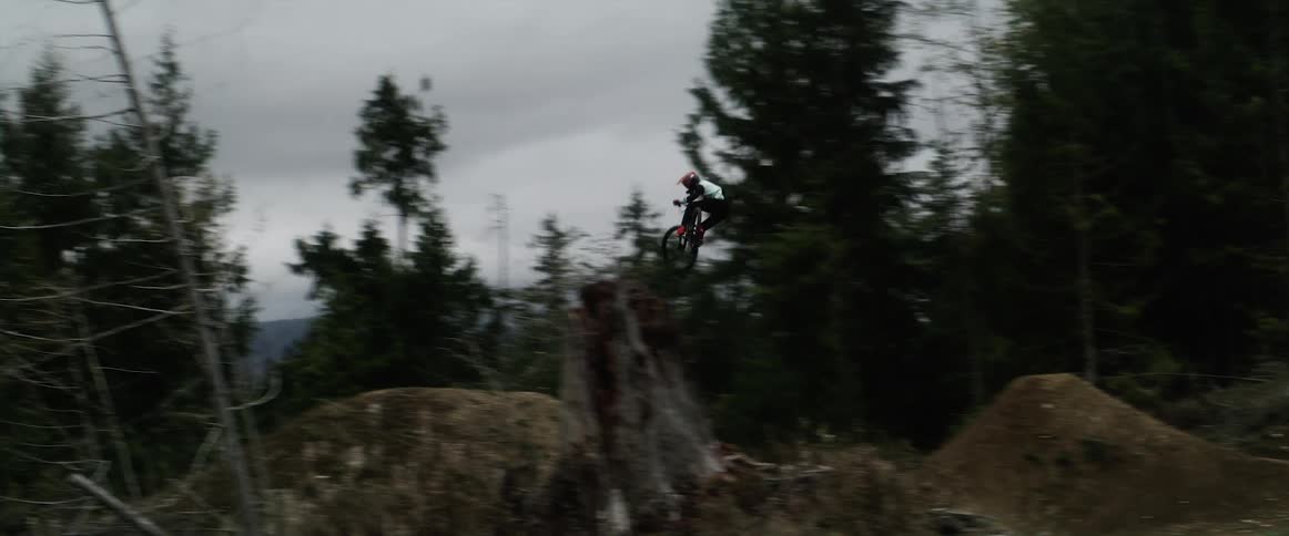 Cyclist rides mountain bike over mounds in clearing near forest jumping each time