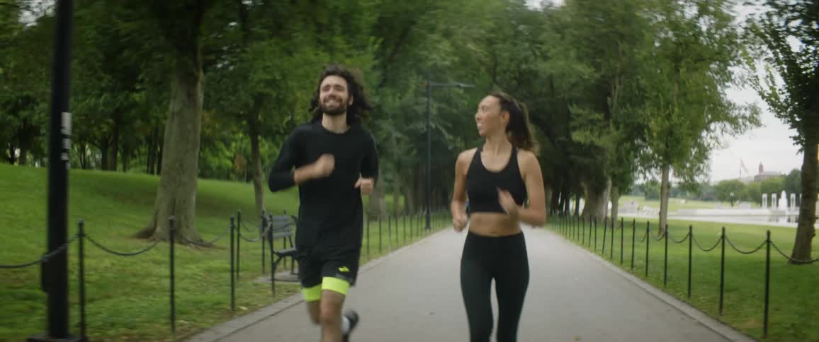 Joggers move along path through park with other joggers and manmade pond in the background