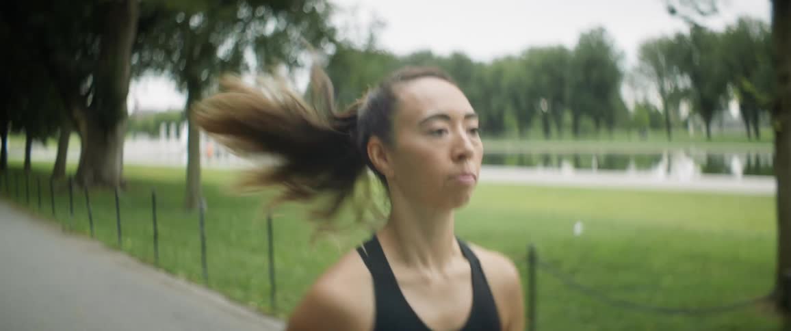 A woman jogs along a pathway through a public park on a cloudy day