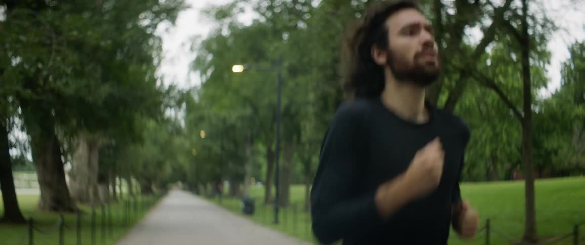 A man with long hair and a beard jogging on a park path