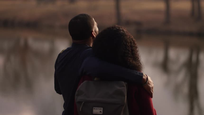 A man stands in front of a river with his arm around a woman