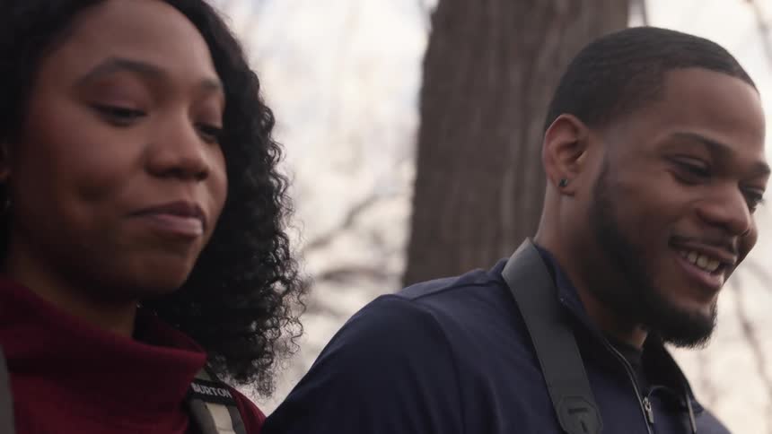 A man and a woman are smiling and talking as they walk near trees