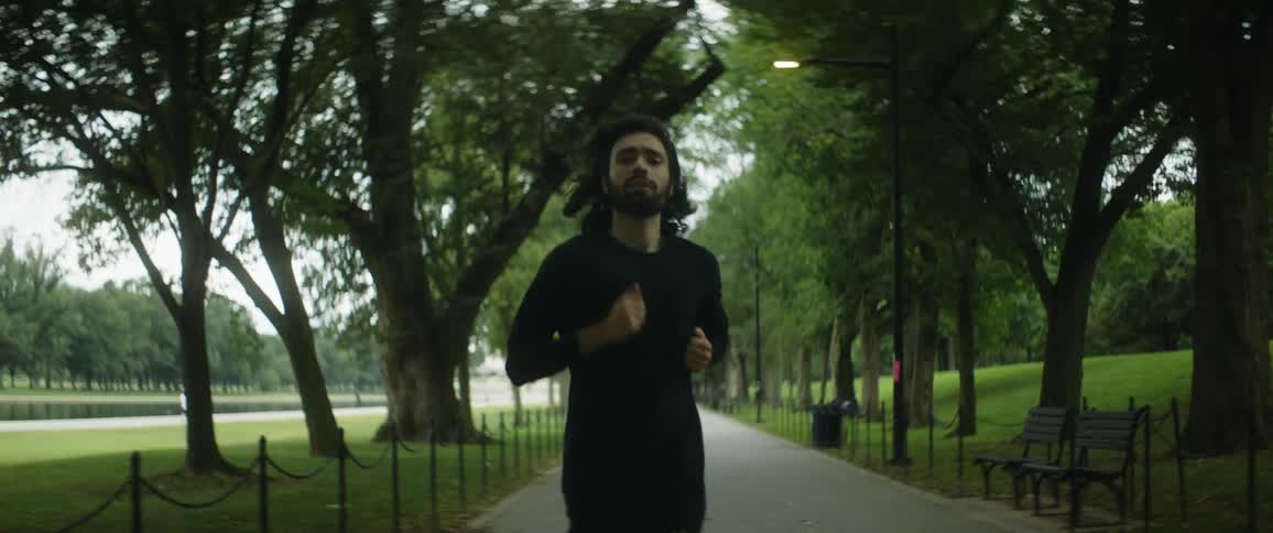 A man is jogging on a walkway between trees in a park