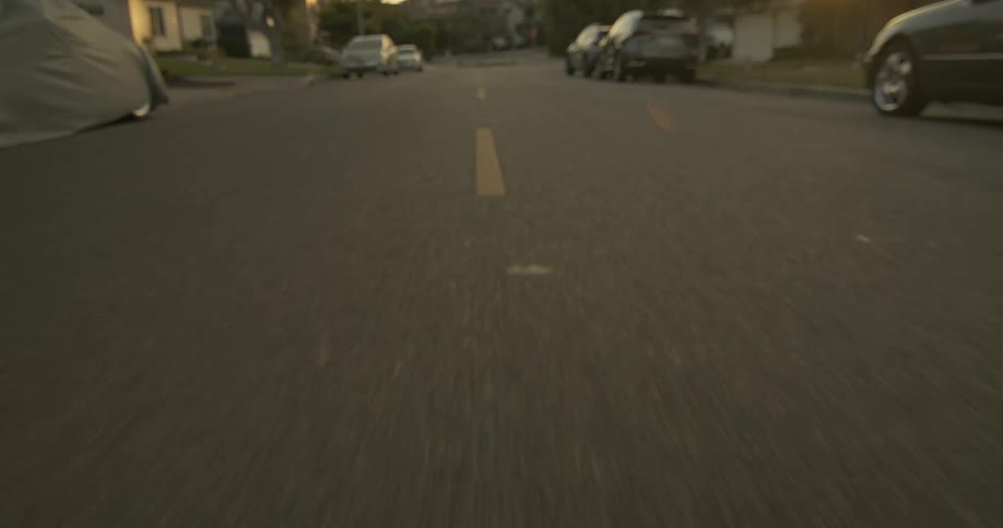 Moving on the middle of a road between rows of parked cars in a calm neighborhood at morning