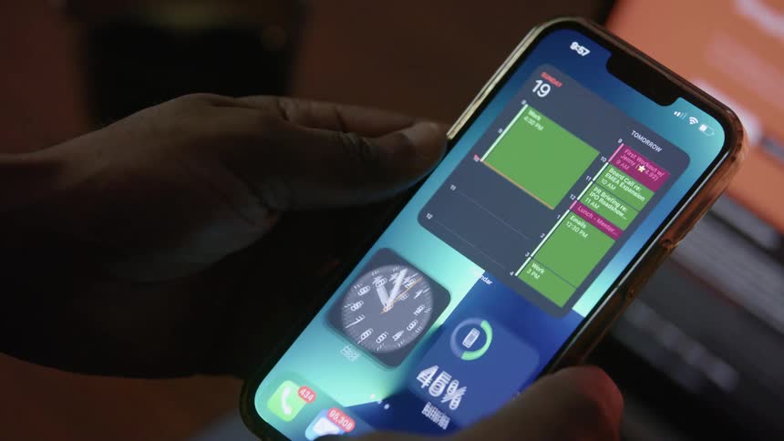 A man picks up his smartphone and turns it on and then looks at his calendar