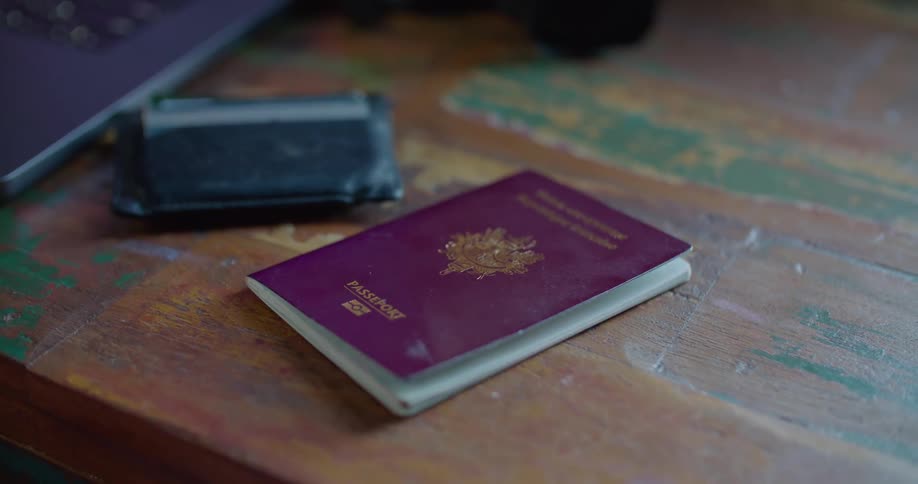 Passport and wallet with credit cards sits on rough wooden surfaced table next to laptop