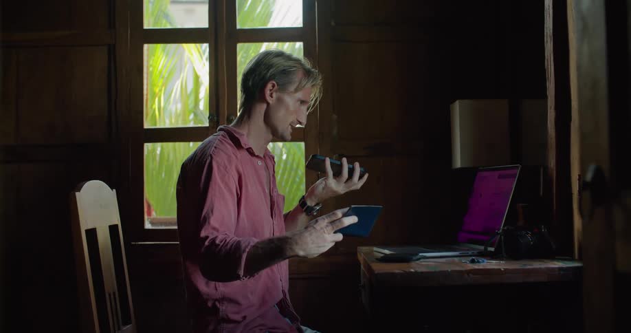 A man reads off information from a passport while talking on speakerphone at his desk