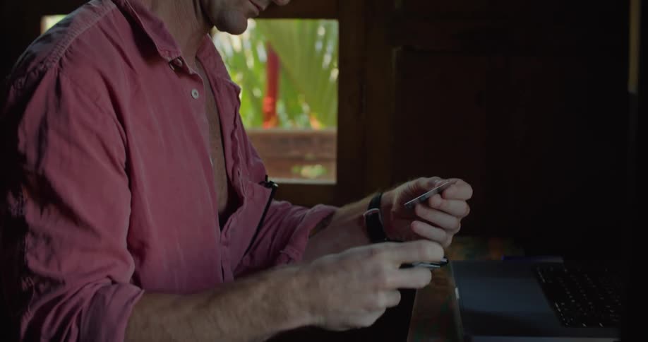 Man turns around a credit card to read the numbers on the back to make an online purchase from the hotel room