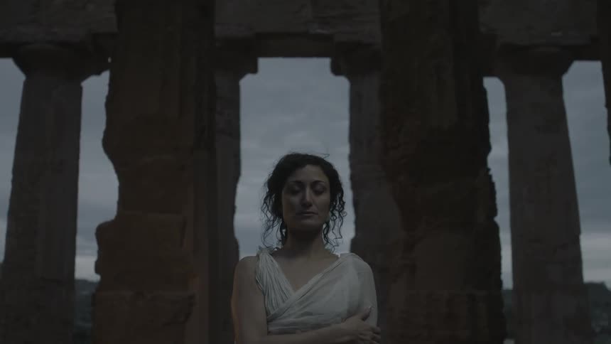A woman standing between columns of the acropolis at dusk