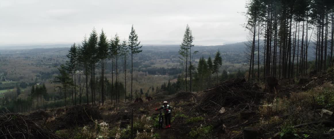 A person walks their mountain bike up a hill in a forest area