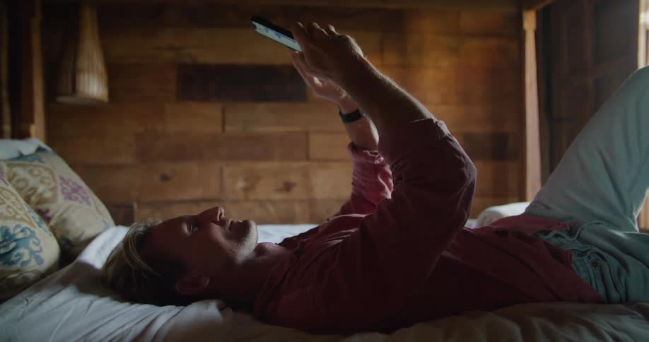 A man uses his smartphone while lying in bed during the day