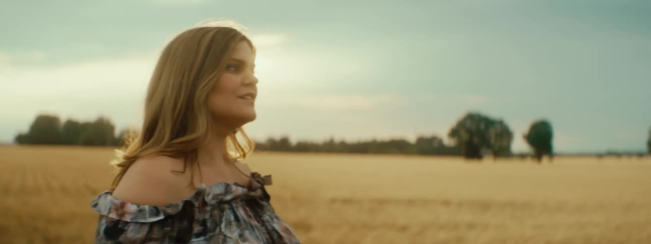 A woman wearing a sundress is walking on farmland as her long hair moves over her shoulders