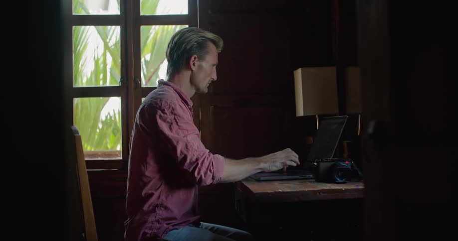 Man sitting at wooden table types on laptop