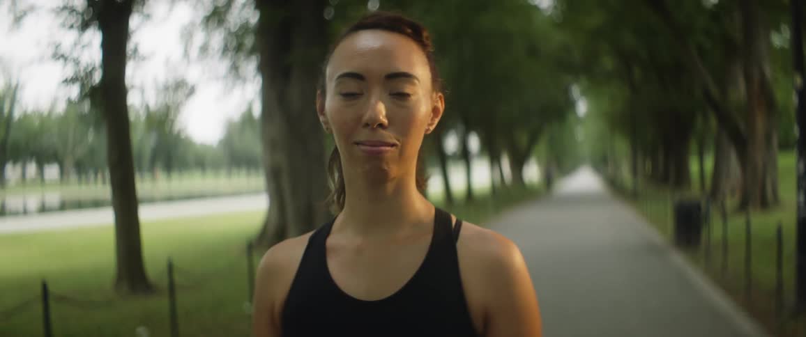 Woman with ponytail and black sports bra looks at camera in public park