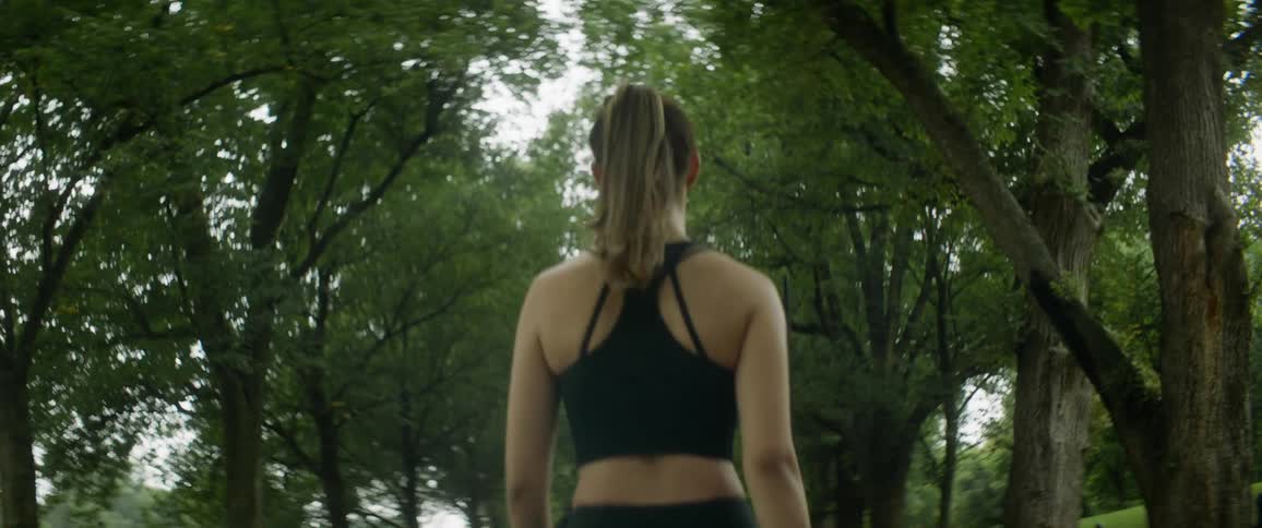 Woman wearing sports top walks along tree lined fenced off path