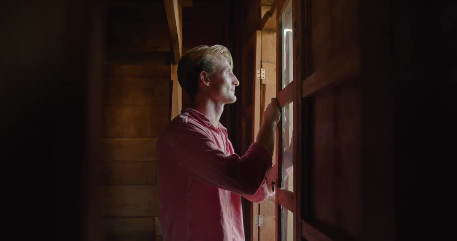 A man is standing indoors and looking out a window
