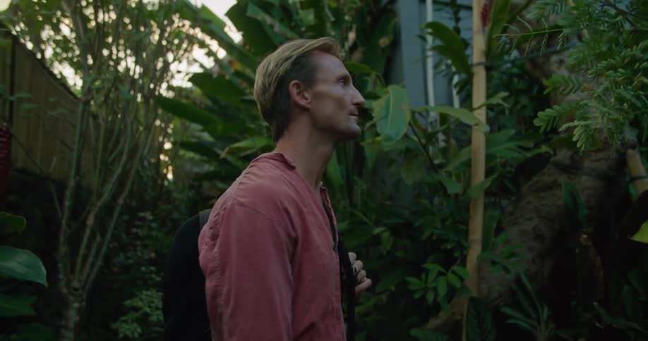 Man with backpack looks around landscaping with a slight smile before walking along path